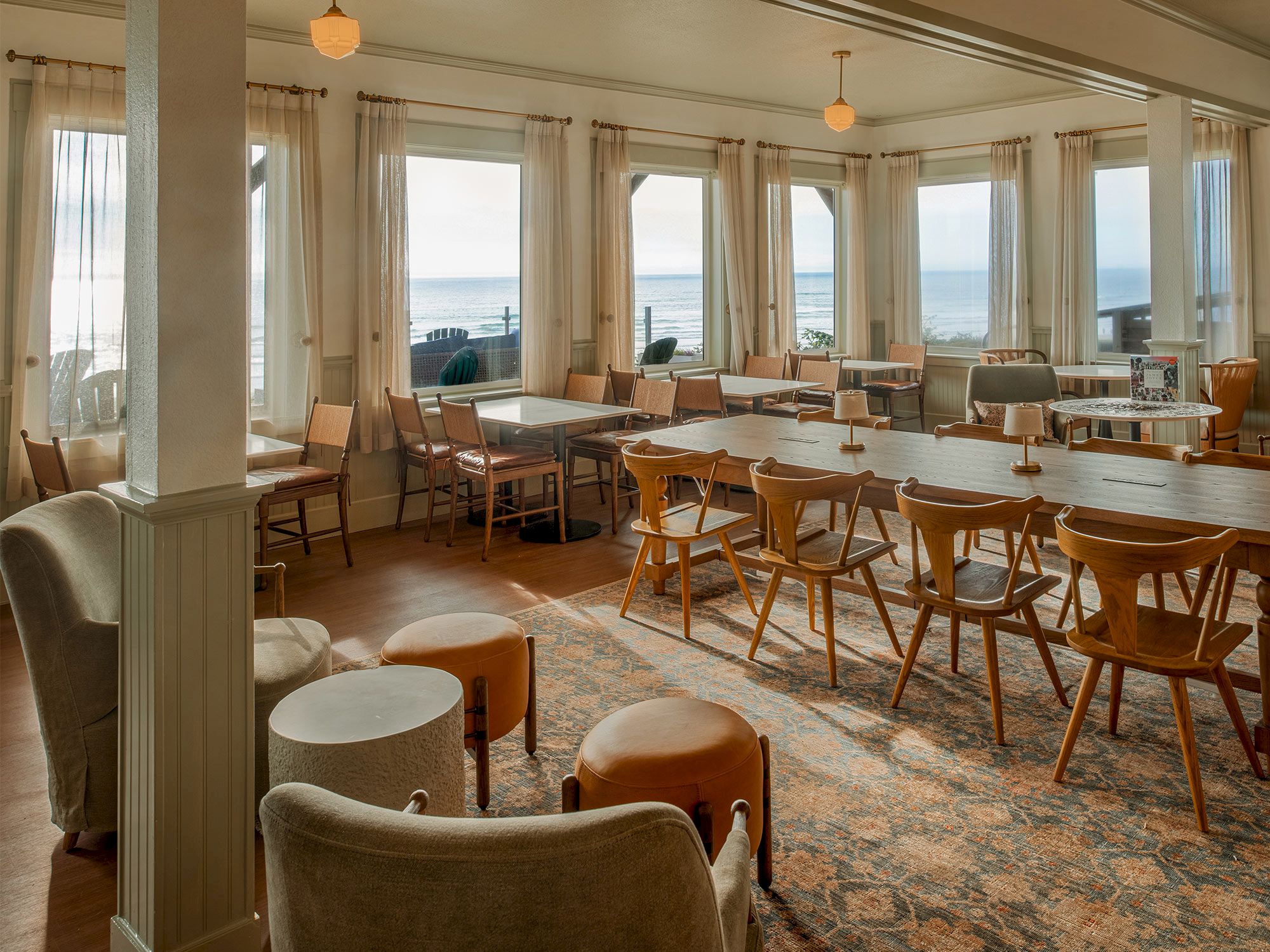 A cozy dining area with wooden chairs and tables, large windows offering a scenic ocean view, and soft lighting enhancing the ambiance.