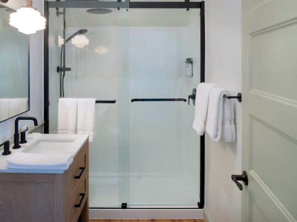 A modern bathroom features a shower with glass doors, a sink with black fixtures, and towels hanging on a rod next to a door.