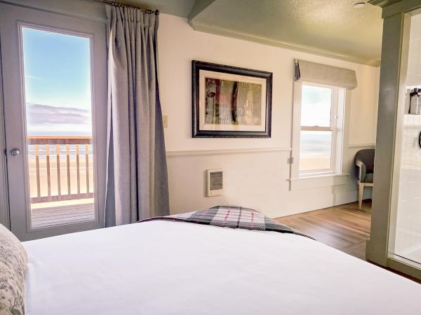 A cozy bedroom with a large bed, ocean view, framed art, and an adjacent glass shower enclosure.