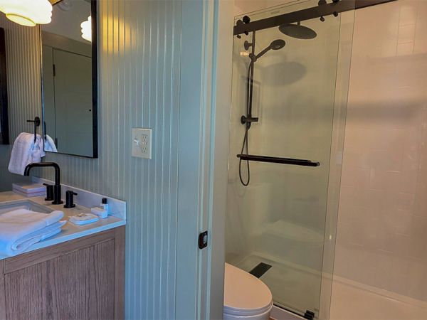 A bathroom with a wooden vanity, a black faucet, towels, a mirror, and a shower with sliding glass doors and dual showerheads.