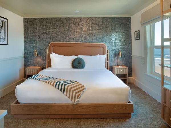 A stylish bedroom with a large bed, decorative wallpaper, bedside tables, and natural light from a window.