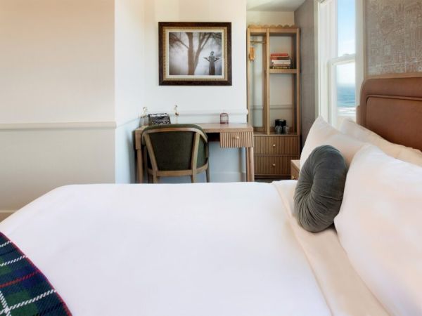 A cozy bedroom with a neatly made bed, desk, chair, framed picture, and shelves, offering a blend of style and comfort.