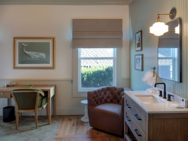 The image shows a cozy room with a desk, chair, armchair, and a sink. There's a window, painting of a whale, and soft lighting.
