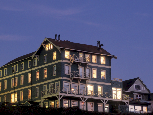 A multi-story building with lit windows and balconies against a twilight sky.