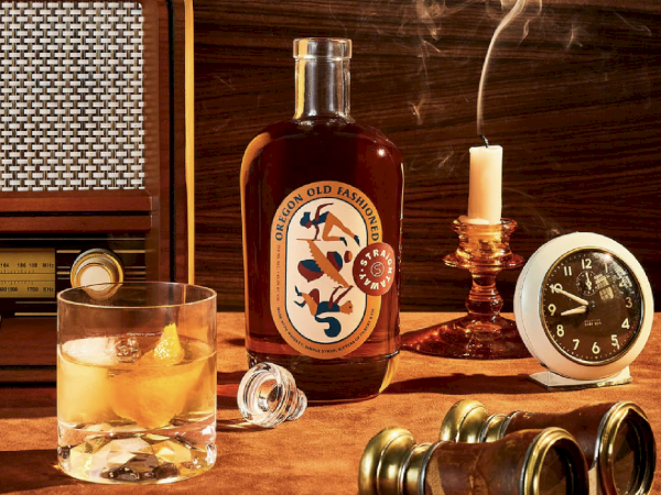 A bottle labeled "Old Fashioned," a glass with ice and drink, a candle, clock, binoculars, and old radio on a wooden surface.