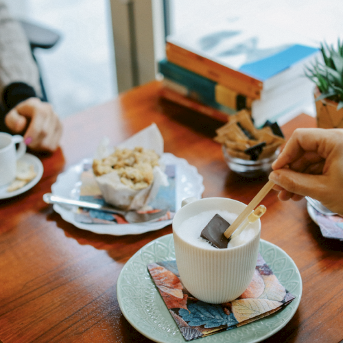 Two people enjoy drinks and snacks at a café table, with books and a plant as decor.