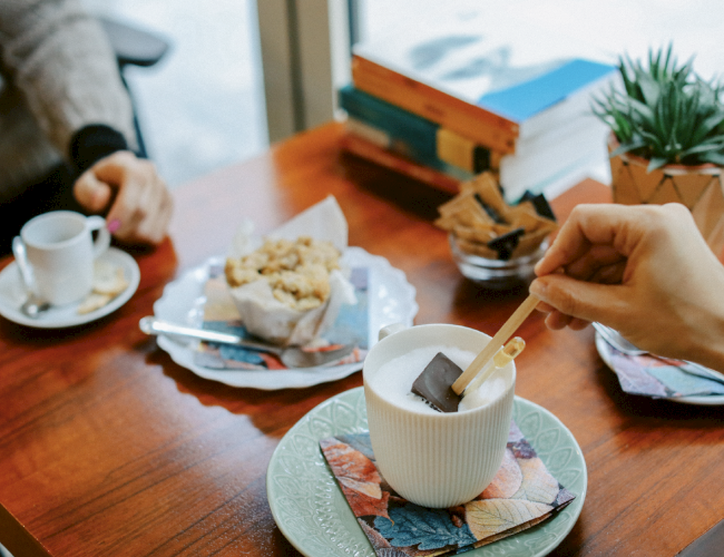 Two people enjoy drinks and snacks at a café table, with books and a plant as decor.