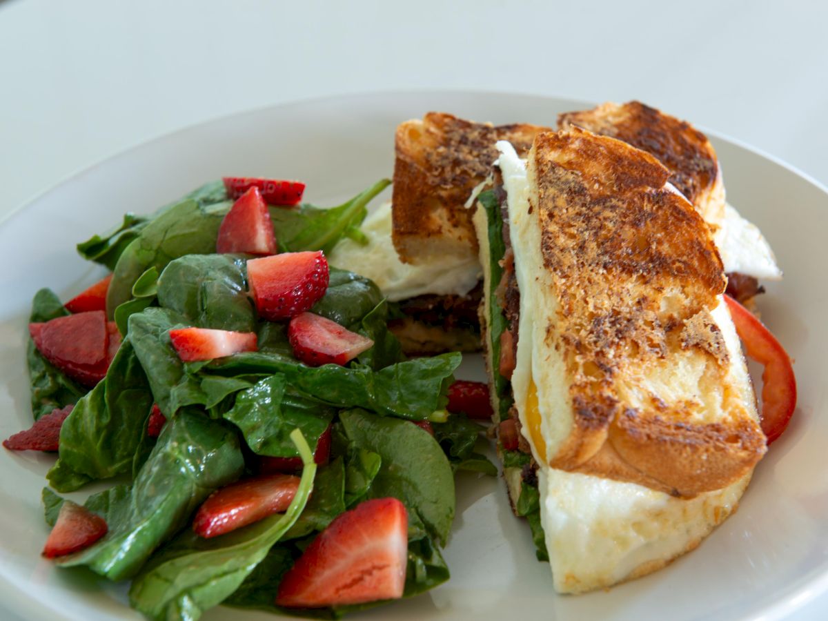 A sandwich with grilled bread and a fresh spinach and strawberry salad on a white plate.