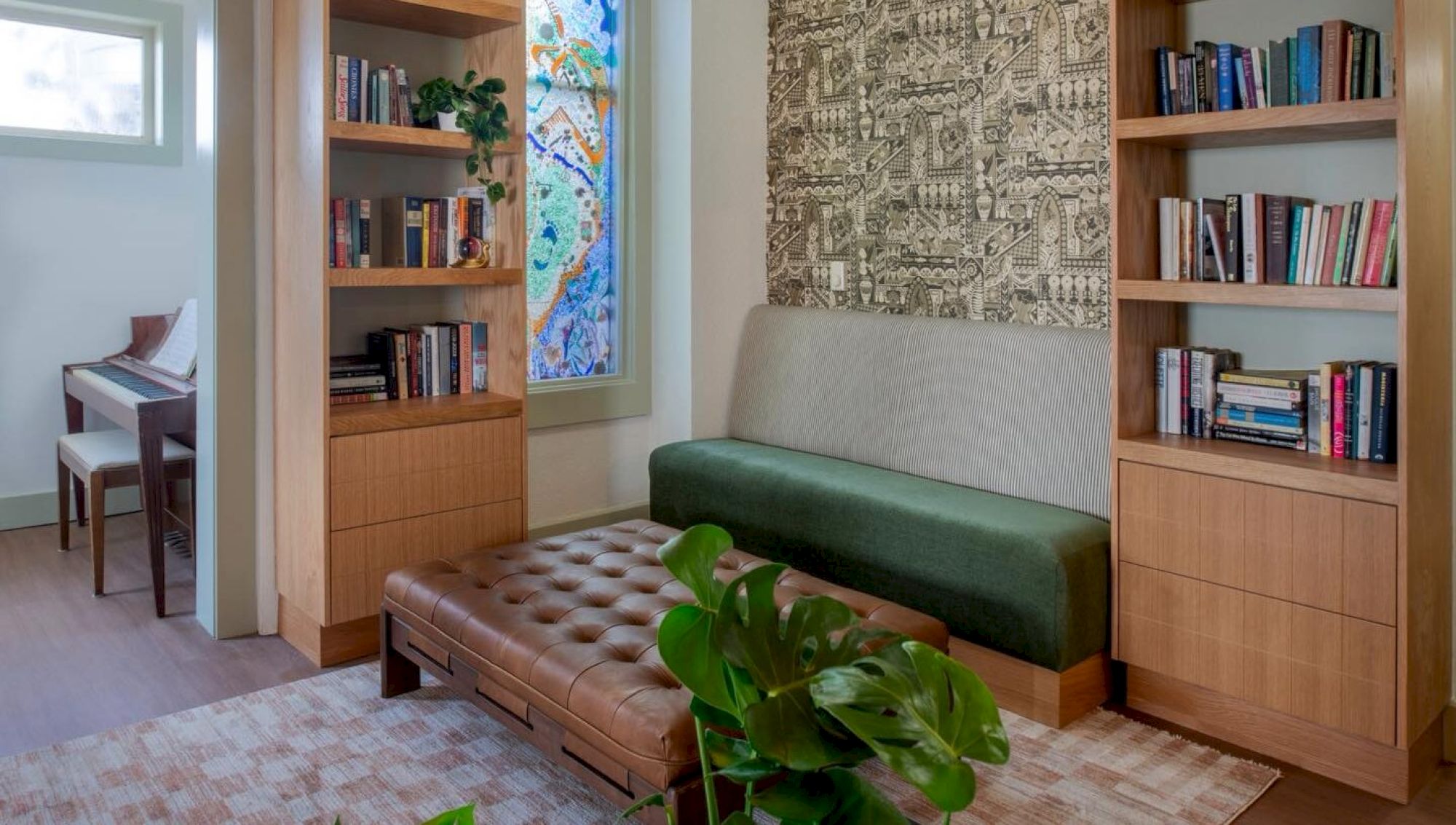 The image shows a cozy room with bookshelves, a green sofa, a brown ottoman, a patterned rug, a plant, and a piano in the corner.