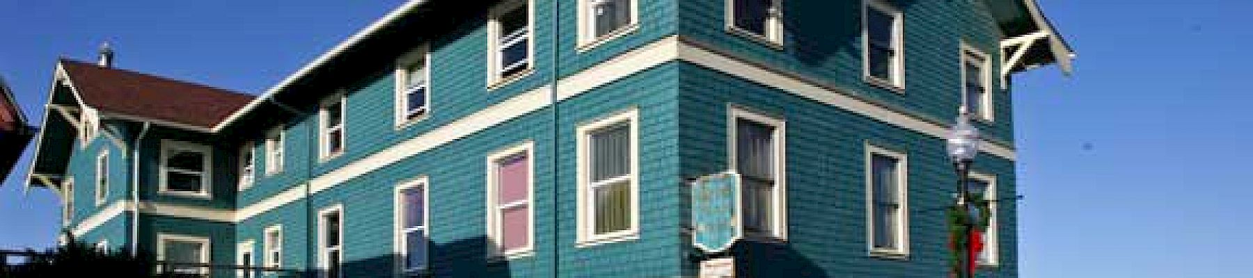 A teal, three-story building with white trim under a clear blue sky, and an old car parked nearby.