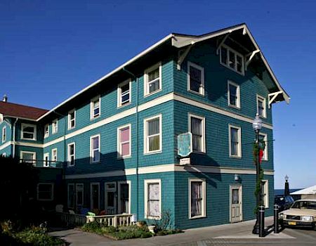 A teal, three-story building with white trim under a clear blue sky, and an old car parked nearby.