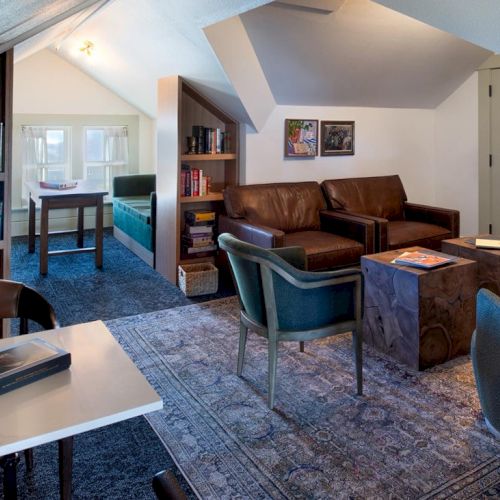 Cozy, wood-accented living room with blue-gray carpet, mid-century inspired seating, built-in bookshelves, and a desk area in a bright, airy attic space.